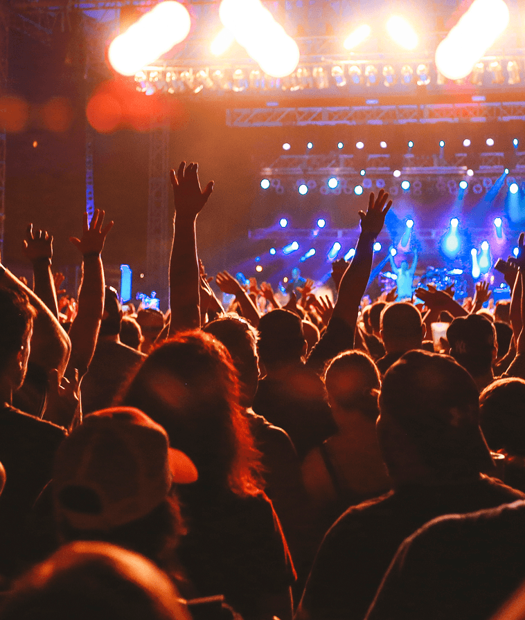 Crowd with raised arms beneath stage lights at a concert.