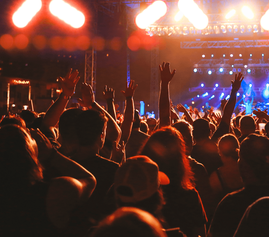 Crowd with raised arms beneath stage lights at a concert.