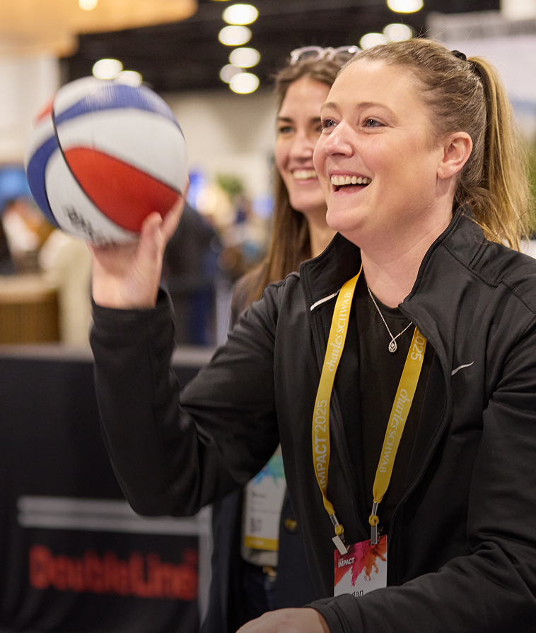 Two women attendees smiling and tossing a ball in The Exchange at IMPACT 2025.