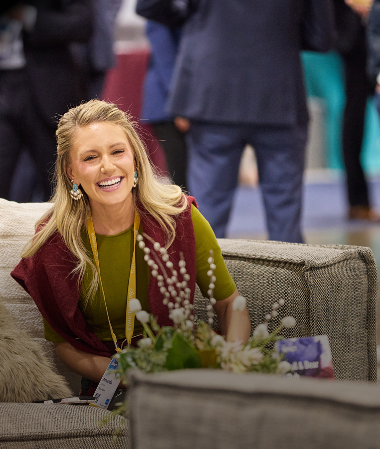 Smiling woman attendee seated in The Exchange at IMPACT 2025.