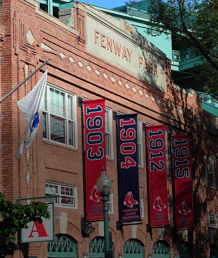 Brick exterior of Fenway Park with championship banners hanging along the facade.