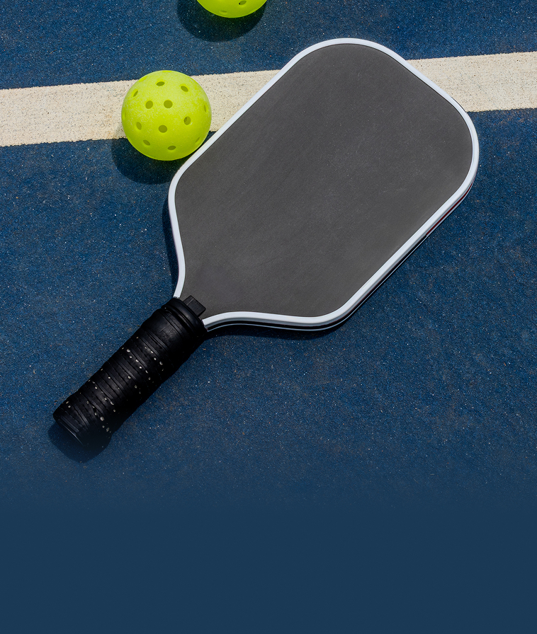 A pickleball paddle and balls resting on an outdoor court.