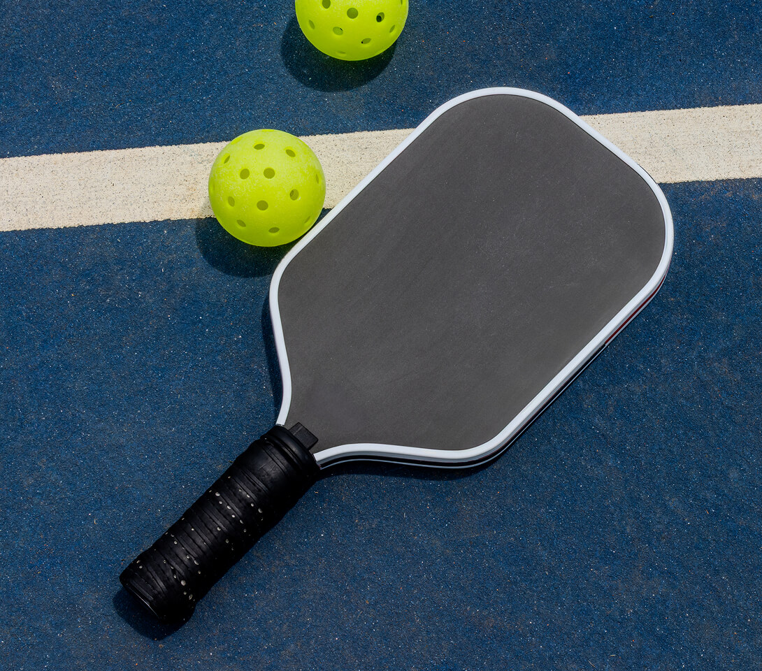 A pickleball paddle and balls resting on an outdoor court.