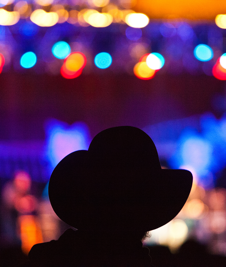 An audience member in a cowboy hat at a music festival. Close up view from the back.