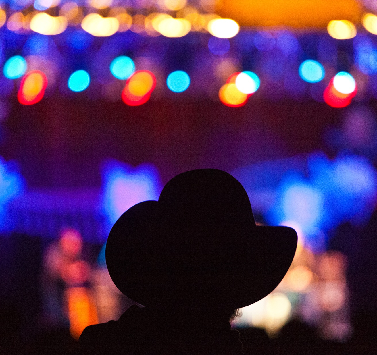 An audience member in a cowboy hat at a music festival. Close up view from the back.