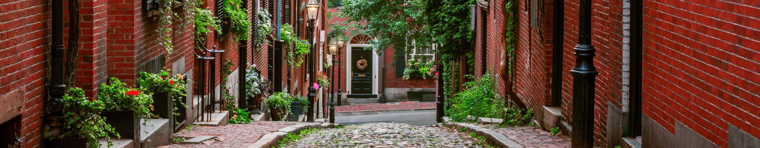Boston, Massachusetts, cobblestone street lined with red brick row houses and greenery.