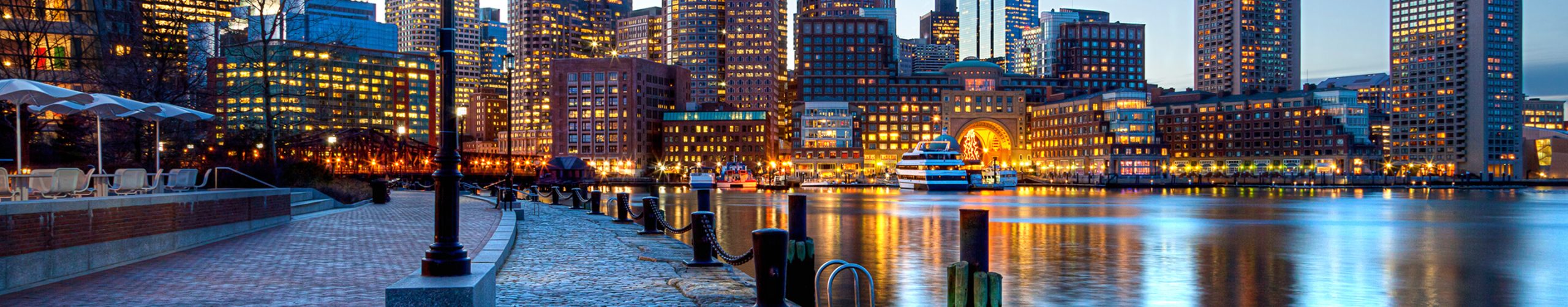 Boston Harbor at night with illuminated buildings in the financial district.