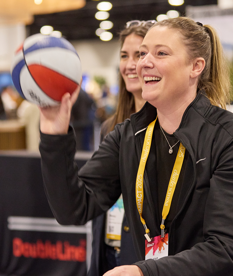 Two women attendees smiling and tossing a ball in The Exchange at IMPACT 2025.