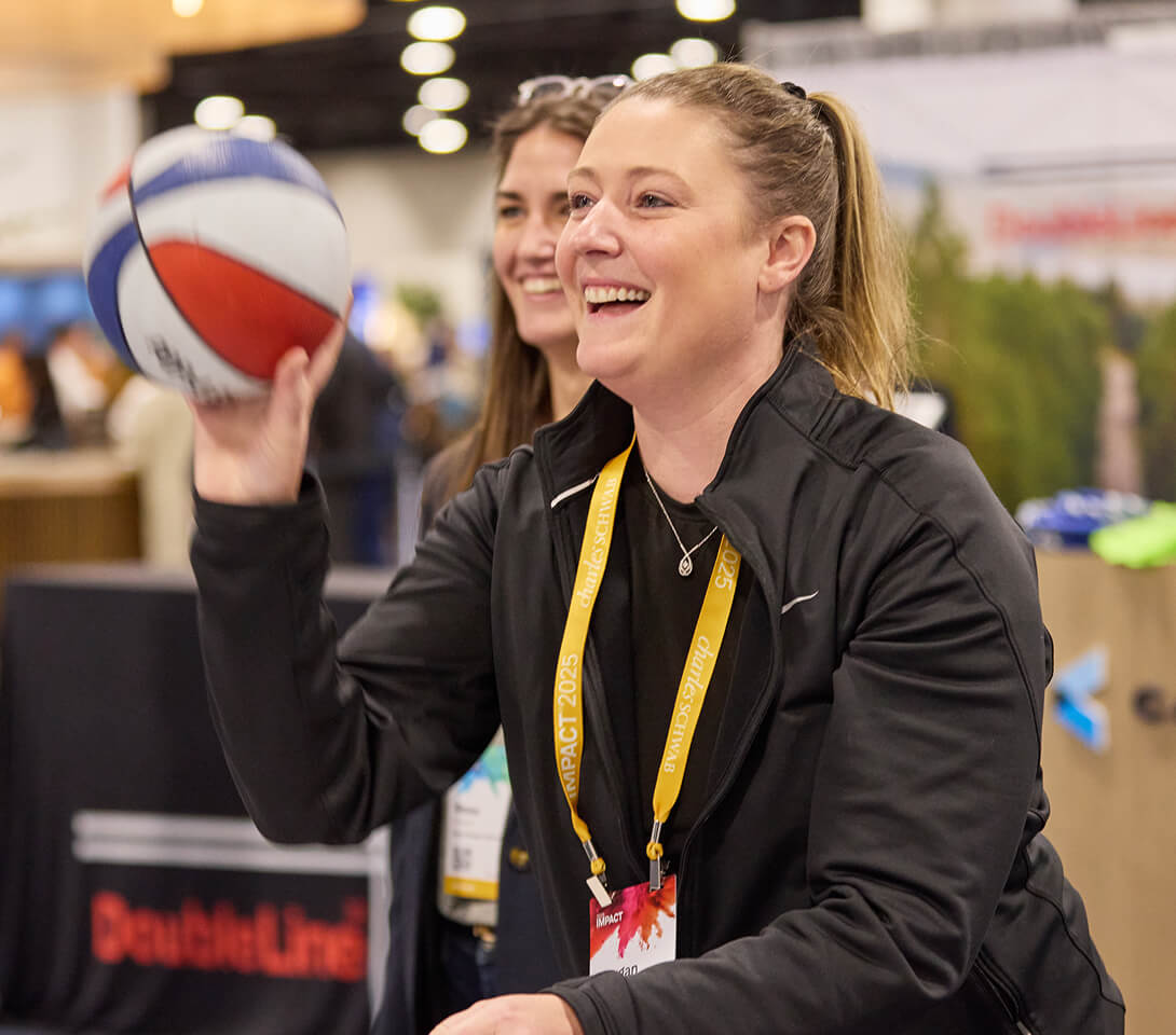 Two women attendees smiling and tossing a ball in The Exchange at IMPACT 2025.