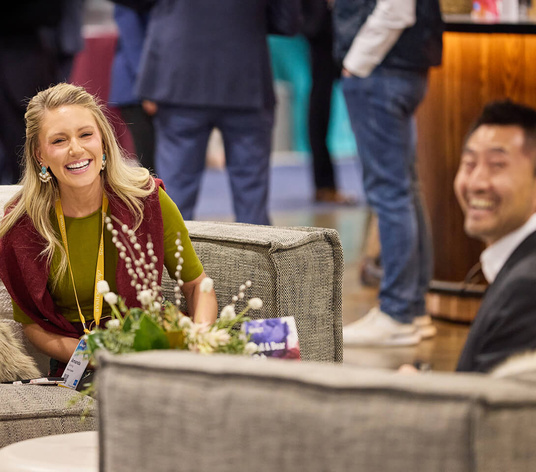 Two smiling attendees seated together in The Exchange at IMPACT 2025.